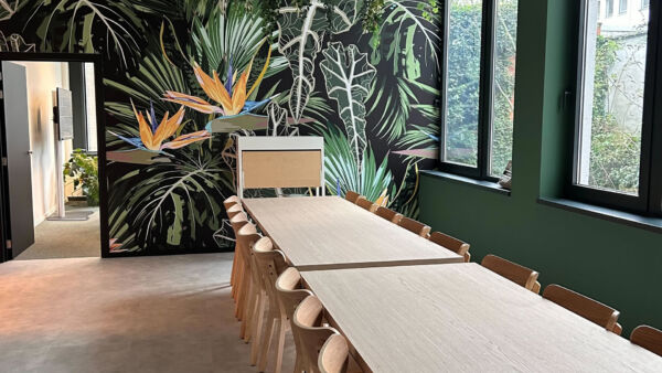 Bright coworking space with a long communal table, wooden chairs, and hanging greenery