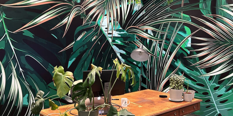 Open-plan coworking area with desks and a tropical bird mural on the back wall