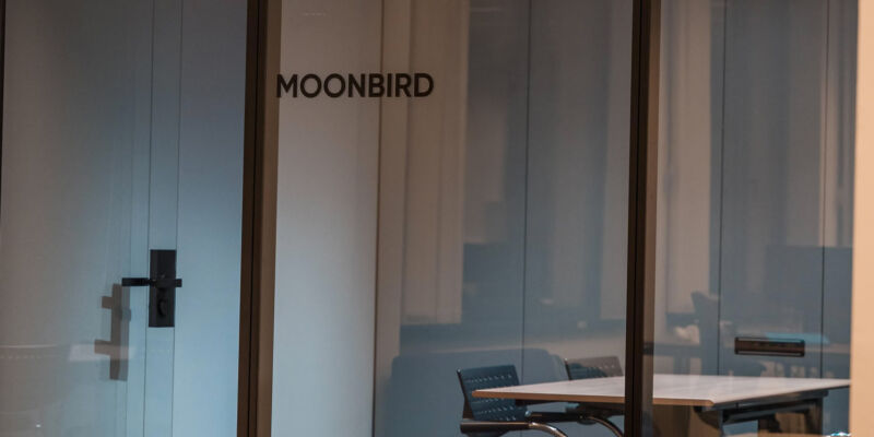 Modern glass-walled meeting room named 'Moonbird' with a table and chairs